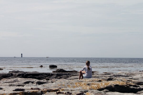 A girl looking at a lighthouse in the ocean