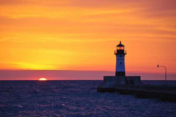 Sea, lighthouse on the background of the departing sun