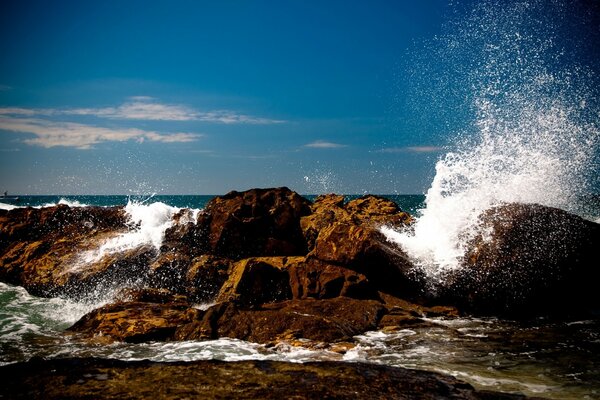 Las olas golpean las piedras contra el fondo del cielo azul