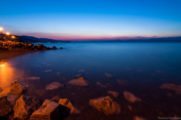 日落时的海湾，黄昏，岩石海岸，夜间度假小镇的灯光