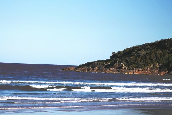 A hill on the ocean shore against a blue sky