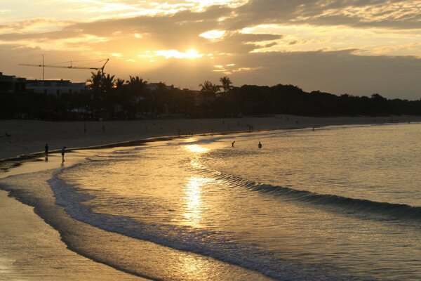 Sonnenuntergang über einem tropischen Strand, leichte Meereswellen überfliegen den Sand