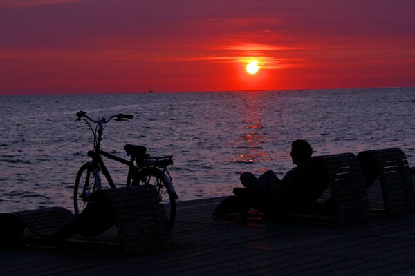 Mann bei Sonnenuntergang am Meer mit Fahrrad