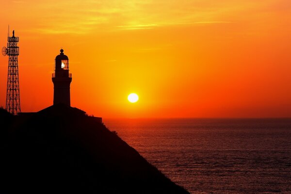 Ein Leuchtturm auf einem Felsen über dem Meer im roten Licht der untergehenden Sonne