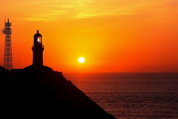 Lighthouse on a rock above the sea in the red light of the departing sun