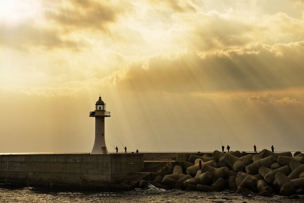 Lighthouse on the background of the setting sun hidden from the clouds