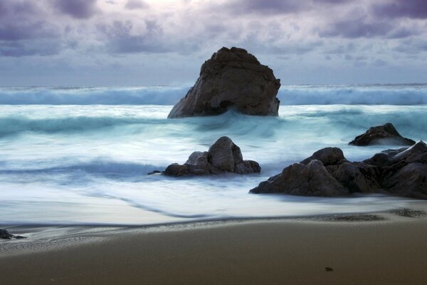 Costa de arena con rocas rocosas contra el mar agitado