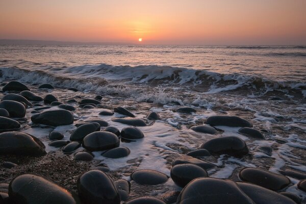 Pôr do sol no oceano e grandes pedras na praia