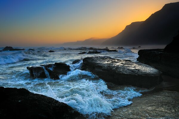 Waves crashing against rocks against the background of sunset