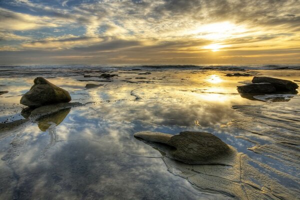 Sonnenuntergang am Meer mit Steinen, die aus dem Wasser geschärft werden