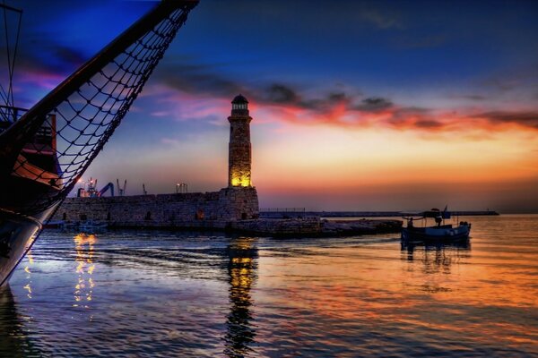 O pôr do sol e o farol são refletidos no mar