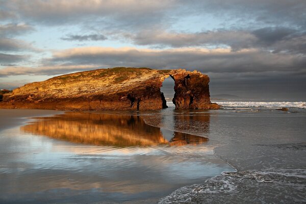 A rock shrouded by ocean waves at sunset