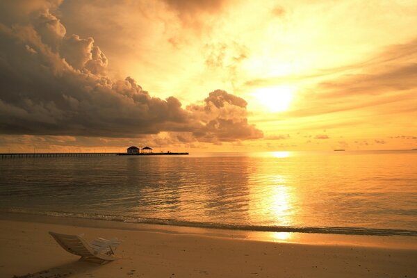 Stimmungsvoller Strand mit Liegestuhl und Meer bei Sonnenuntergang