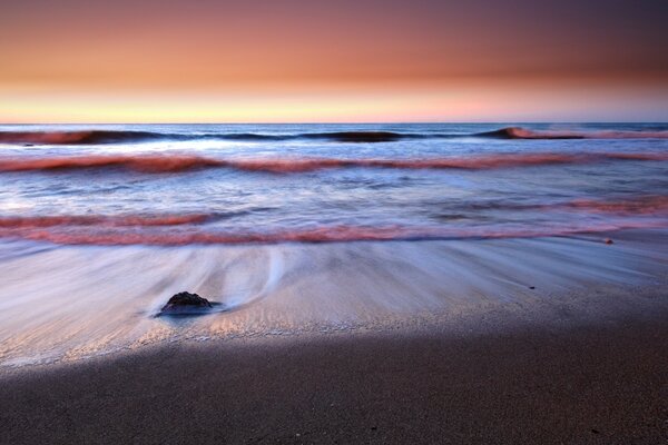 Riflusso sulla spiaggia di sabbia e tramonto