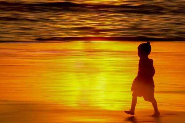 Criança andando na praia ao pôr do sol