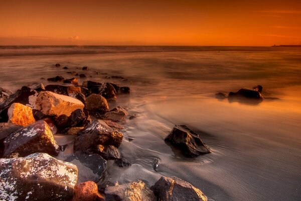 Grandi massi nella sabbia si estendono nell acqua di mare al tramonto giallo-rosso