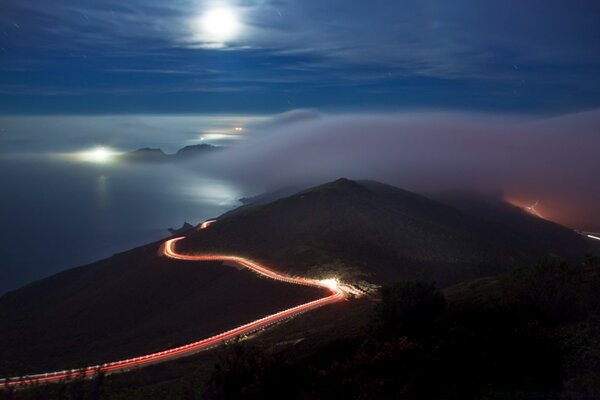 Largo camino iluminado a través de las montañas y el mar