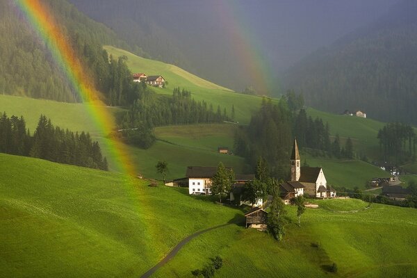 Bellissimo prato estivo con arcobaleno sullo sfondo di case