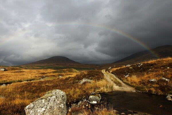 A landscape of mountainous terrain with a gloomy sky and a rainbow