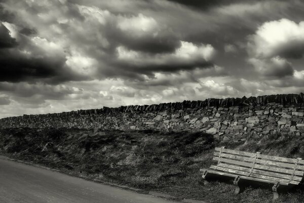 Paisaje en blanco y negro banco y carretera en primer plano detrás de muchas rocas arriba cielo con nubes