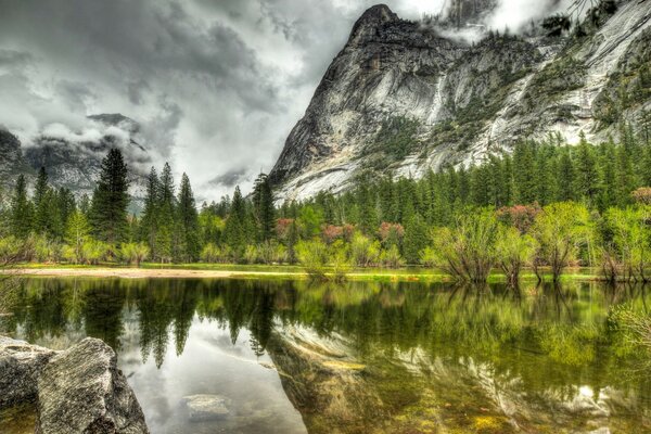 Reflection of the forest and mountains in the lake against the gray sky