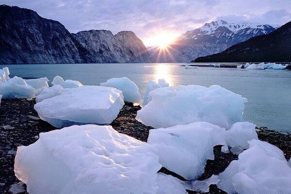 Blocks of ice in the sunlight against the background of mountains and water