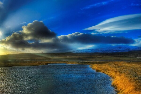 Der Teich ist von Feldern mit gelbem Gras und einem Himmel mit Wolken umgeben