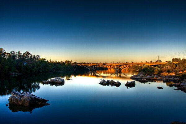 Ein Fluss mit einem reflektierenden blauen Himmel und einer Brücke in der Ferne