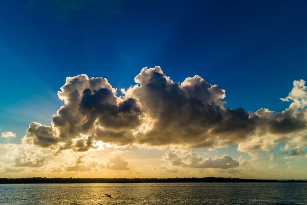 The sun is behind the clouds near the water