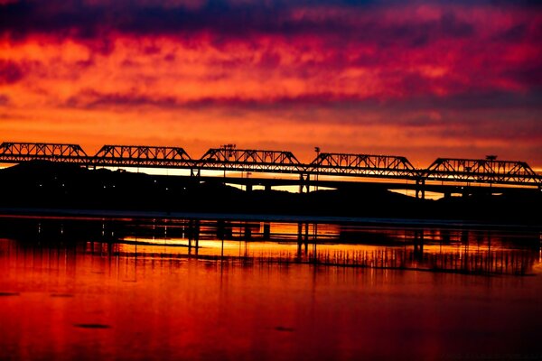 In the reflection of the water, the bridge is visible against the background of sunset