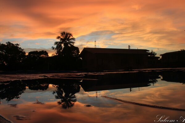 The silhouette of houses with palm trees in the eternal sky reflected in the water