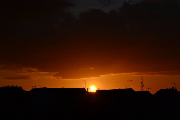 Der Sonnenuntergang verbirgt sich hinter dunklen Häuserdächern am leuchtend orangefarbenen Himmel