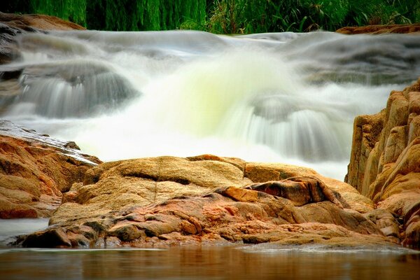 Wasserfall auf dem Hintergrund von Steinen und Fluss