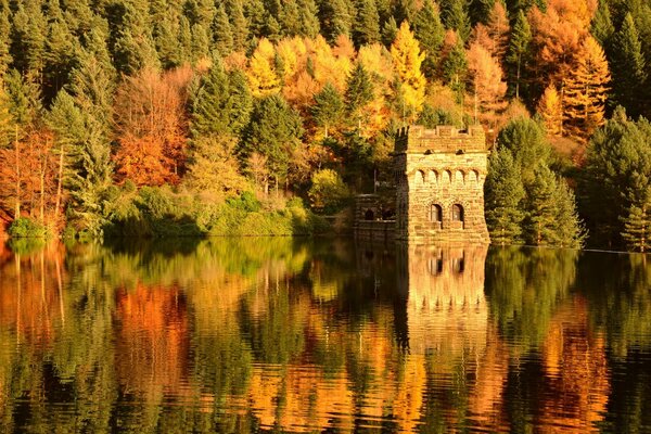 An old building against the background of an autumn forest. reflection of the autumn forest in the water