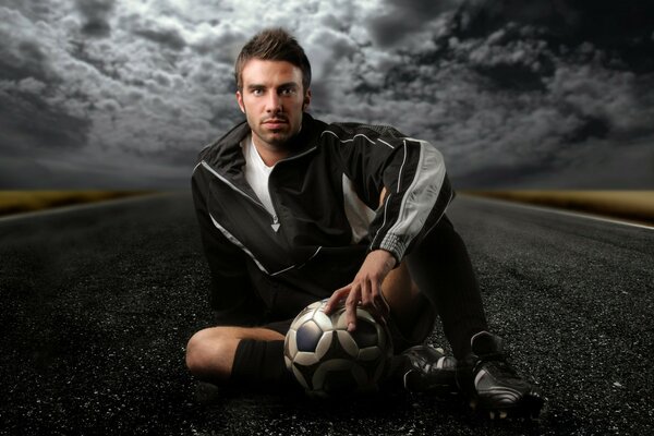 A man is sitting on the road with a ball in his hand