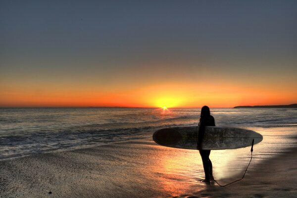 Chica surfista acompaña a la mirada puesta de sol al atardecer