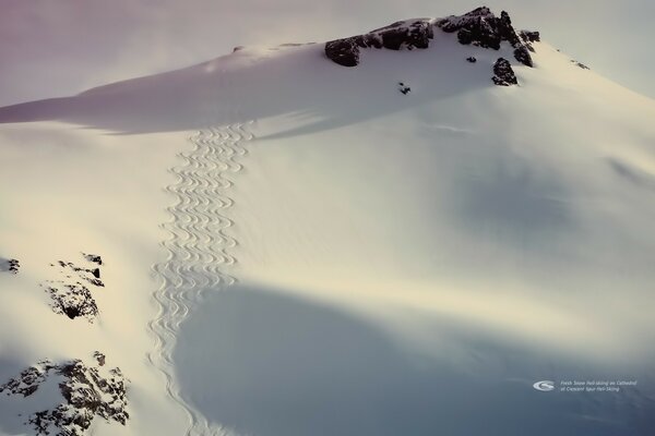 Snowy mountain slope in the rays of the sun with curly footprints in the snow