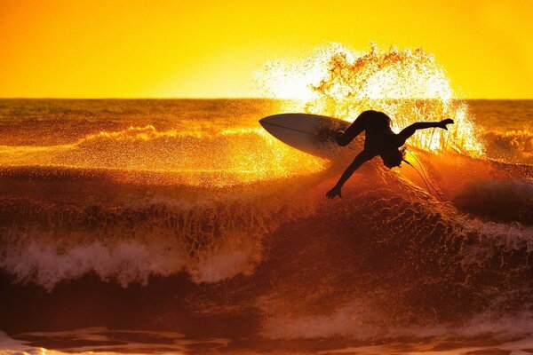 Ein Surfer steht bei Sonnenuntergang auf einem Brett im Meer