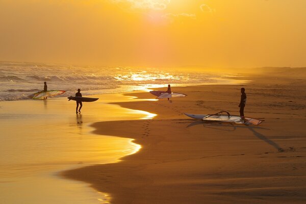 Personas con surf en la orilla de la playa de arena al atardecer