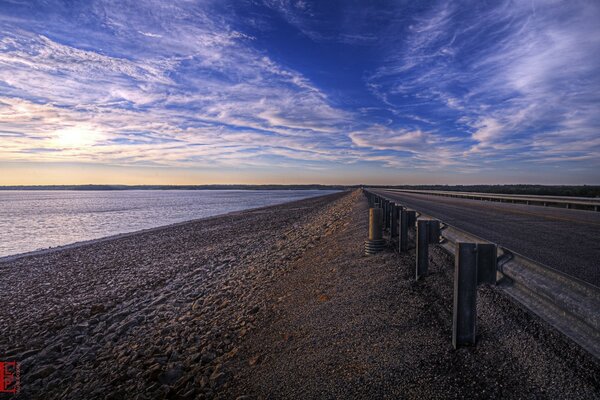 A road running along a rocky beach on the background of sunset