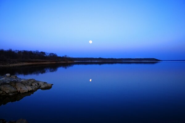 The moon is reflected in a calm lake