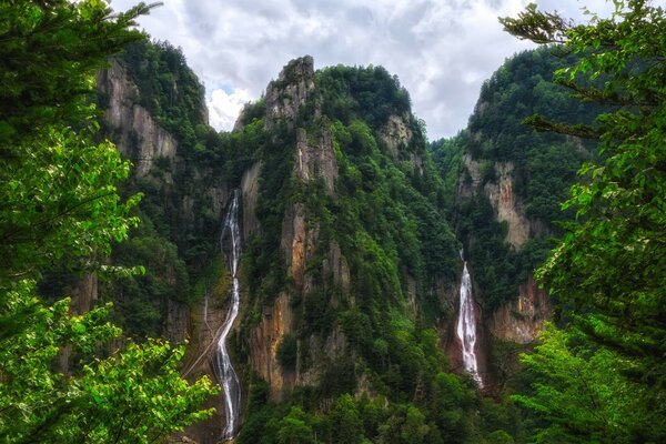 घने वनस्पति और एक झरने के साथ पर्वत श्रृंखलाएं