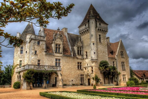 Gotisches Schloss auf Himmelshintergrund und Blumenbeeten