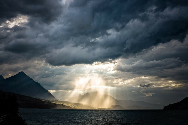 Mountains and a lake illuminated by the rays of the sun, which looks out from the clouds