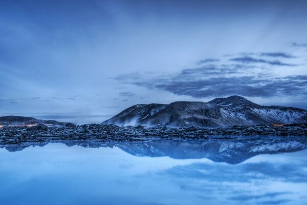 A snow-covered mountain range by the water at dusk