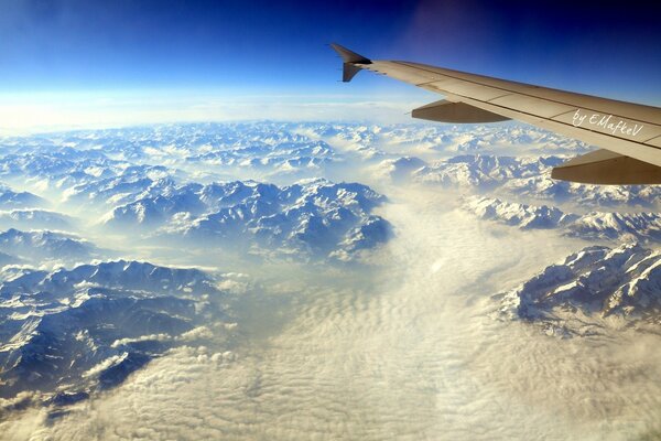 Sob a asa do avião, as montanhas ficam brancas( aparentemente, os Alpes), porque ele dirigiu o caminho para a Europa