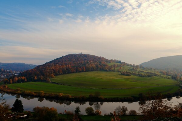 Herbstliche Landschaft. Wald, grünes Feld, Fluss