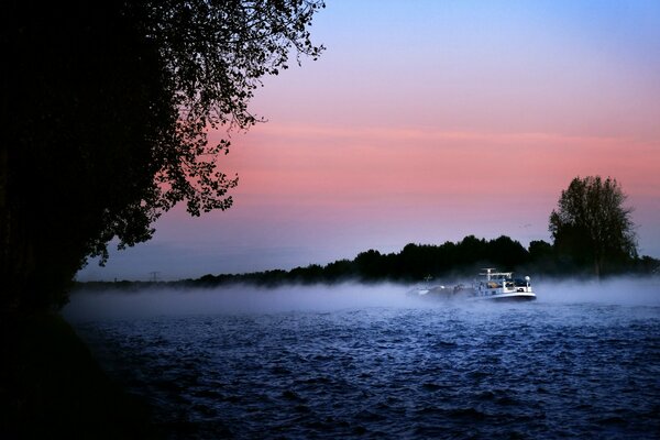 Nevoeiro da manhã sobre o rio com um navio